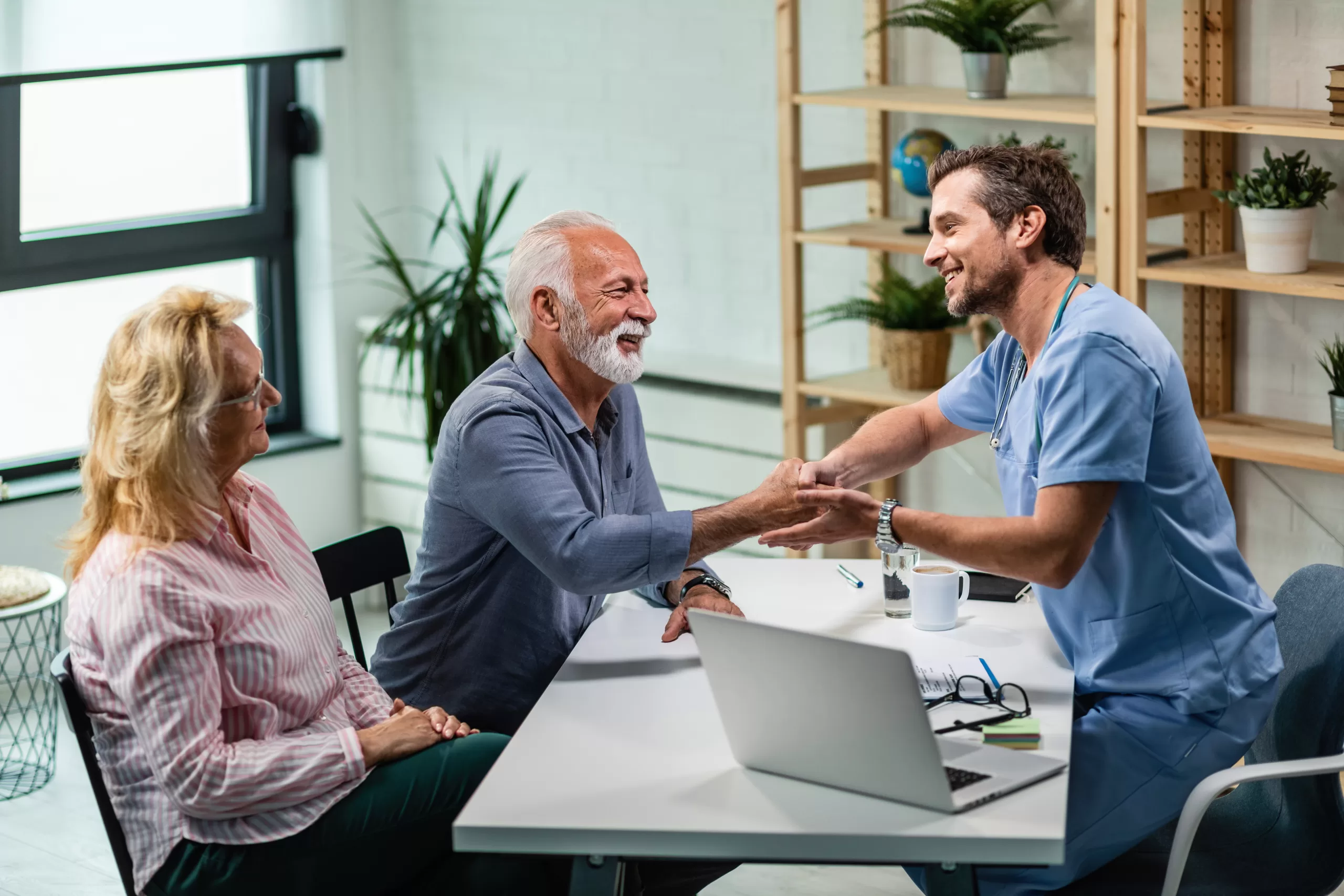Happy male doctor shaking hands with senior man who came to medical appointment with his wife.